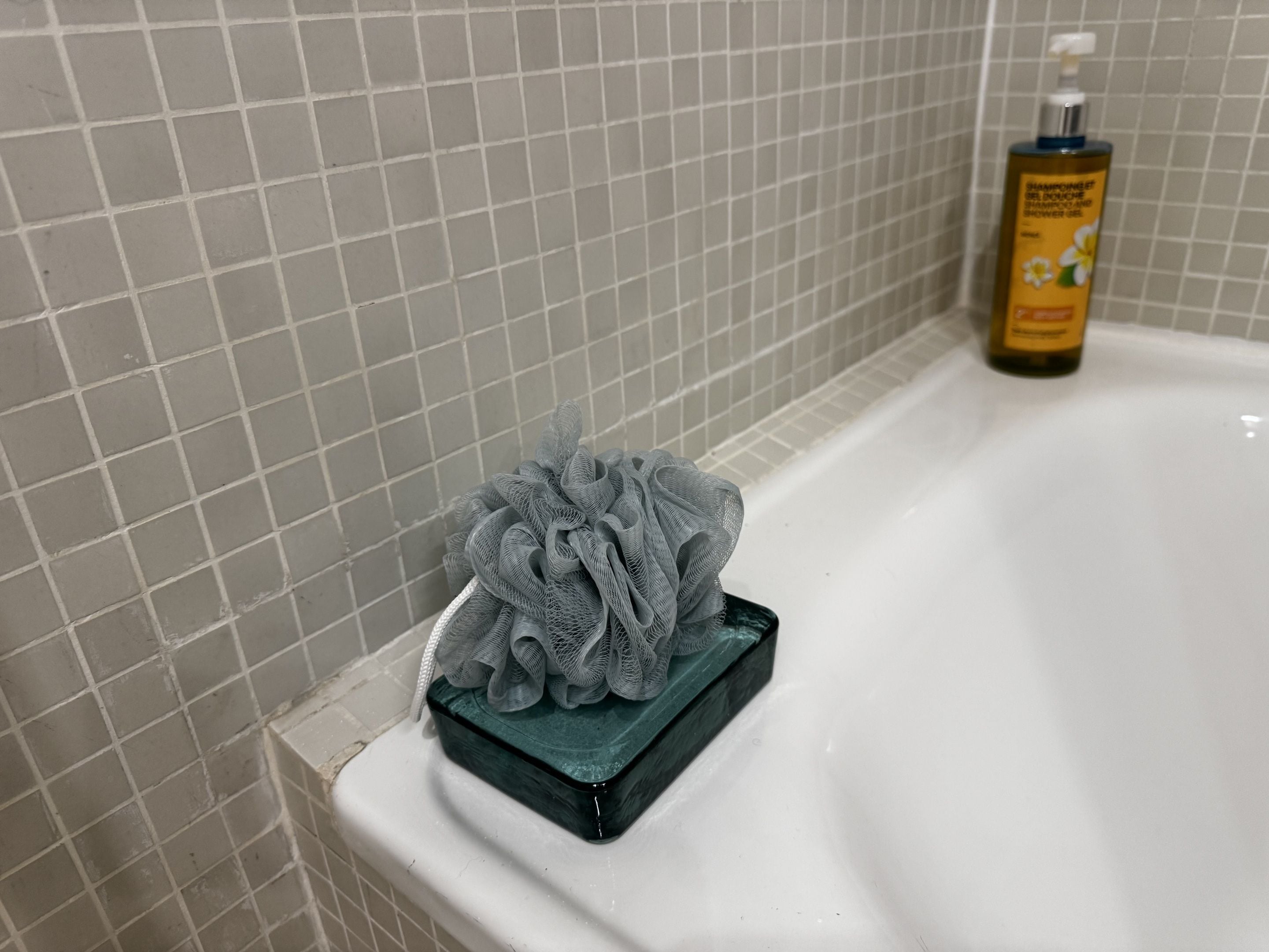 Un baño con una bañera blanca, un cabezal de ducha gris y una botella de champú.