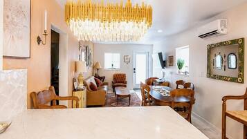 A modern kitchen with a marble countertop, a chandelier, and a dining area with wooden furniture.