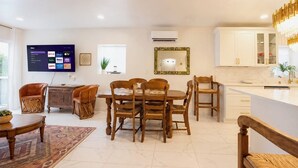 Un soggiorno moderno con televisione a schermo piatto, arredi in legno e angolo cottura con mobili bianchi.