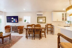 A modern living room with a flat-screen TV, wooden furniture, and a kitchen area with white cabinets. - Cultural NM home close to UNM Plex, NHCC, Downtown, Zoo, Barelas (Albuquerque)