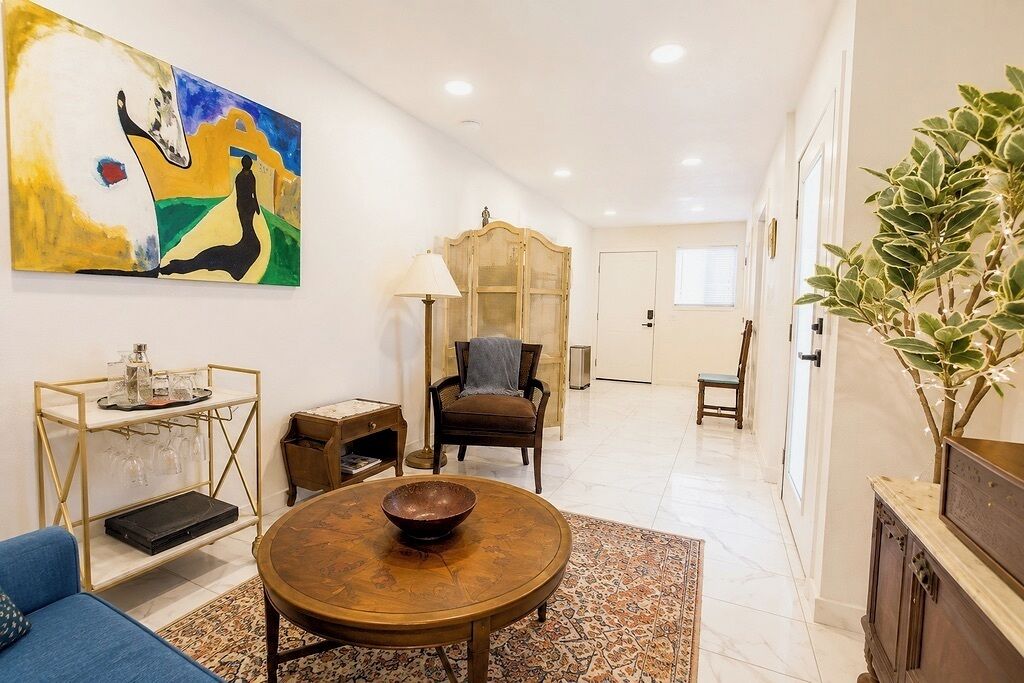 A spacious living area with a round coffee table, a sofa, a wooden cabinet, a painting, and a potted plant.