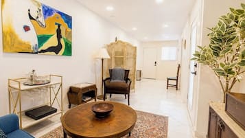 A spacious living area with a round coffee table, a sofa, a wooden cabinet, a painting, and a potted plant.