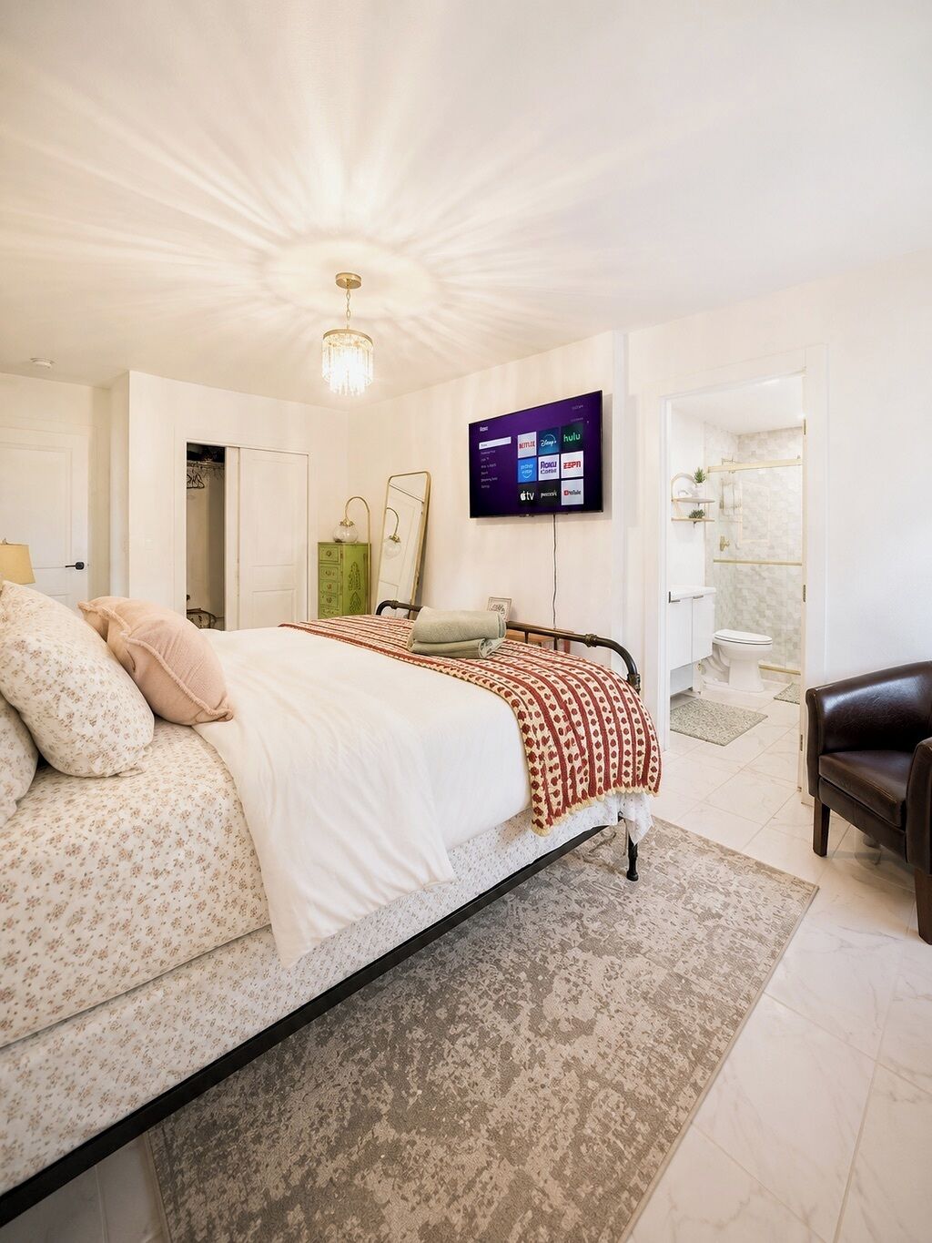 Ein Schlafzimmer mit Bett, einem an der Wand montierten Fernseher, einem Badezimmer mit Dusche und einer Tür zu einem weiteren Zimmer.