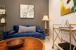 A blue sofa with a patterned pillow, a wooden coffee table, a gold-framed side table with a lamp, and a wall-mounted painting. - Cultural NM home close to UNM Plex, NHCC, Downtown, Zoo, Barelas (Albuquerque)