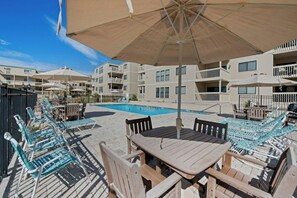 Un espace aménagé au bord de la piscine, avec des chaises longues, une table et des parasols.