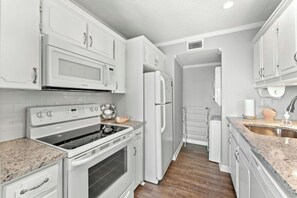 A modern kitchen with white cabinetry, a built-in oven, a microwave, and a refrigerator. - Ocean Bridge C1- Beach Across The Street- 2BR (Myrtle Beach)