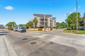 A multi-story residential building with balconies, a parking area, and a clear sky. - Shorewalk 5- 2 Bedroom- Beach Across The Street (North Myrtle Beach)