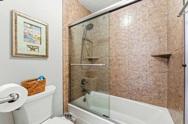Et badeværelse med en brusekabine med glasvægge, toilet og et billede i ramme på væggen.