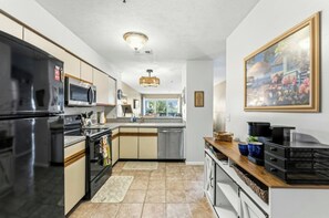 A modern kitchen with a refrigerator, microwave, and stove. There is a dining area with a table and chairs. - Shorewalk 5- 2 Bedroom- Beach Across The Street (North Myrtle Beach)