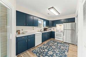 A modern kitchen with blue cabinets, white appliances, and a patterned rug. - Watergate- 4 Bedroom beach House in Cherry Grove (North Myrtle Beach)