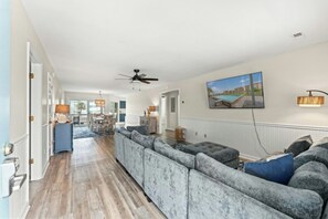 A spacious living area with a long sofa, a ceiling fan, and a dining area in the background. - Watergate- 4 Bedroom beach House in Cherry Grove (North Myrtle Beach)