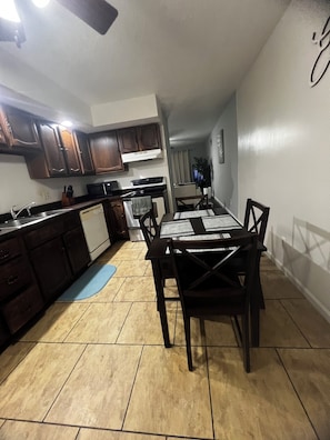 Una cocina con armarios de madera oscura, una estufa blanca y una mesa de comedor con sillas.
