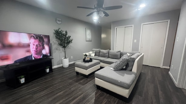 A modern living room with a flat-screen TV, a large potted plant, a grey sectional sofa, and a ceiling fan. - Beautiful 2-bedroom apartment near malls and restaurants in Springfield (Springfield)
