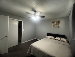 Un dormitorio con cama, ventilador de techo, una puerta y una lámpara fijada a la pared.