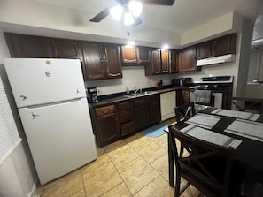 A kitchen with wooden cabinets, a white refrigerator, a microwave, a stove, and a dining table with chairs. - Beautiful 2-bedroom apartment near malls and restaurants in Springfield (Springfield)