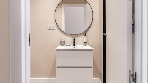 A bathroom with a white vanity, a round mirror, and a bottle of lotion. - Waou Madrid Rio II - Short-Term Rental (Madrid)