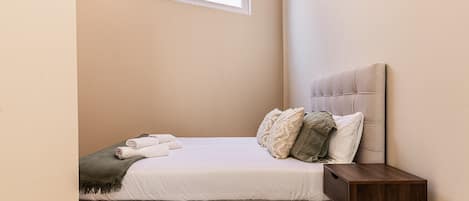 A neatly made bed with a headboard, a bedside table, and a window above.