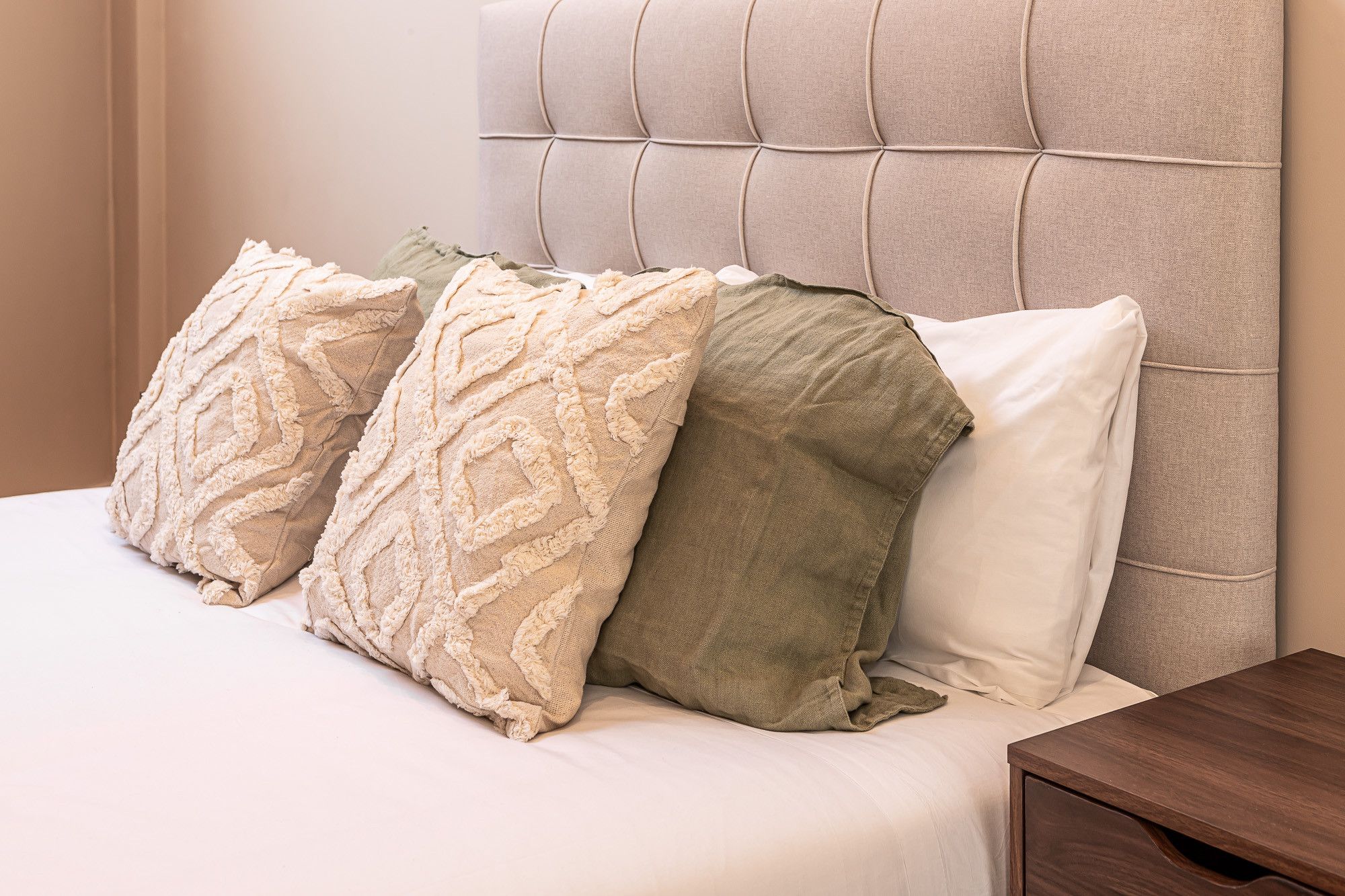 Una cama con cabecera, varias almohadas y una mesita de noche de madera.