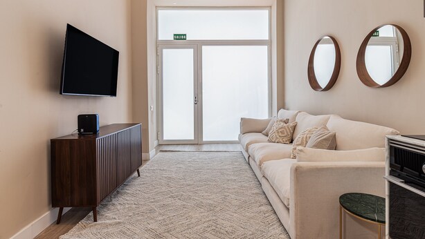 A hotel lobby with a flat-screen TV, a wooden cabinet, a beige sofa, a patterned rug, and a large glass door with a 'SALIDA' sign. - Waou Madrid Rio II - Short-Term Rental (Madrid)