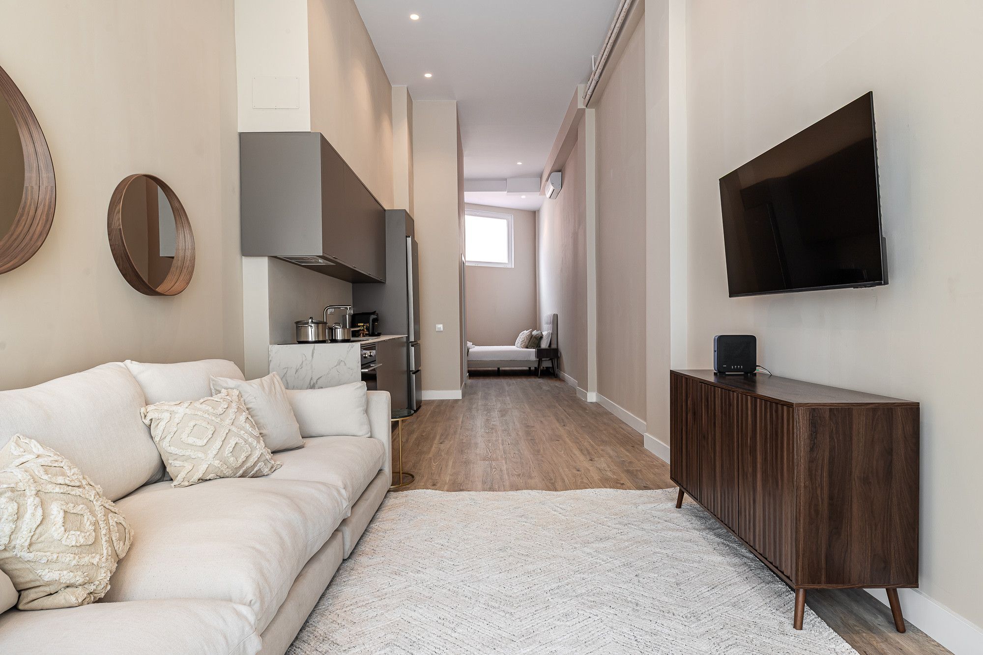 Un interior moderno con sofá, televisión, zona de cocina y un pasillo.