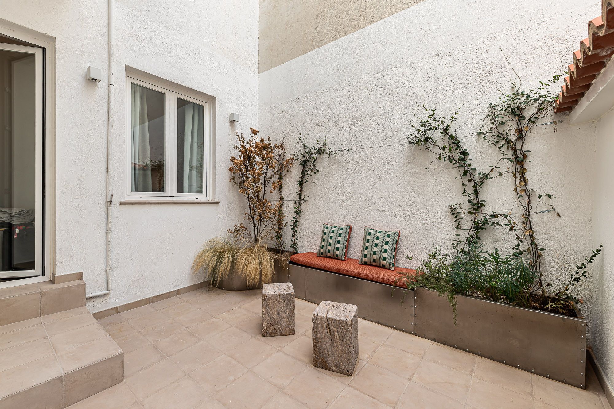 A courtyard with a bench, potted plants, and a window.