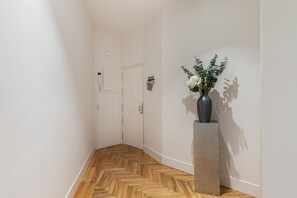 Ein Flur mit Holzdielen im Fischgrätmuster, eine Vase mit Blumen auf einem Sockel und eine Tür mit dem Schild 'HOME'.