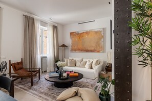 Ein Wohnzimmer mit Sofa, Couchtisch und Sesseln. An der Wand hängt ein großes abstraktes Gemälde und rechts steht ein Blumentopf.