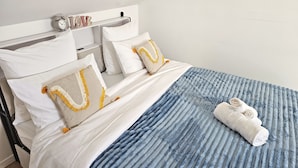 A neatly made bed with white bedding, a blue textured blanket, and two pillows with tassels. - Creil 10 min · Paris, CDG 25 min · Asterix 20 min · JW Assembly 2 min (Creil)