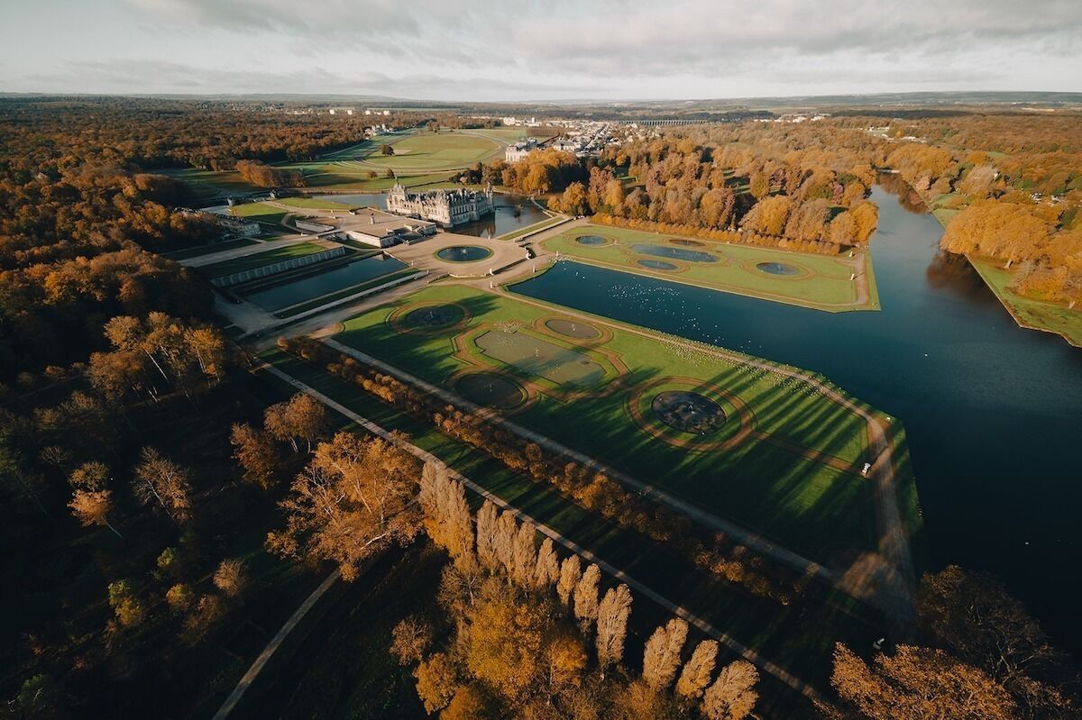 Ilmakuva puistosta, jossa on linna, järvi ja ympäröivät puut.
