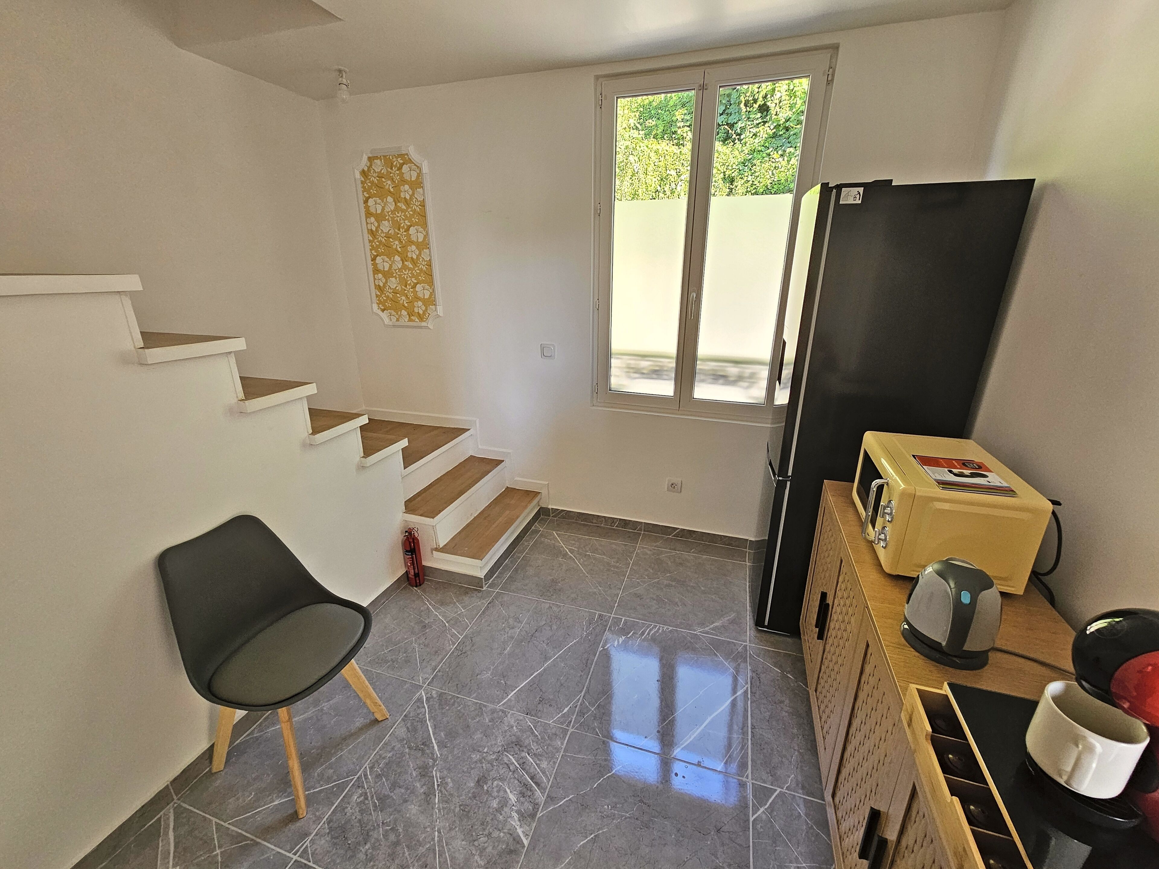A small, clean room with a staircase, a chair, a refrigerator, and a coffee maker.