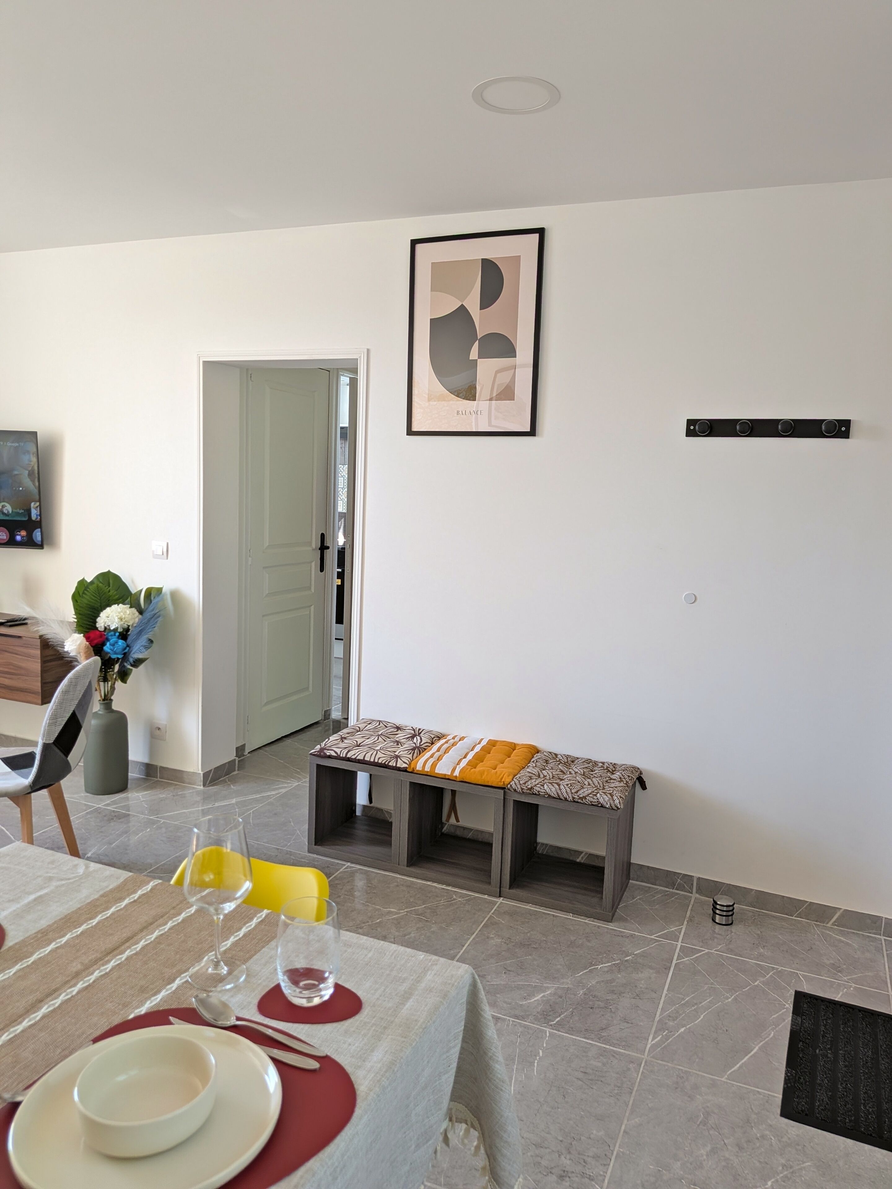 A dining area with a table set for two, a bench, and a framed artwork on the wall.