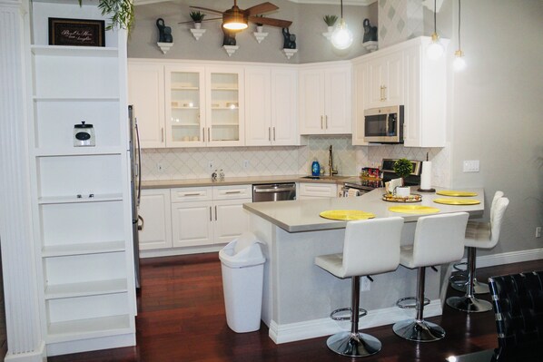 A modern kitchen with white cabinetry, a central island with bar stools, a microwave, and a ceiling fan.