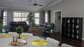 Uma sala de estar com ventilador de teto, dois sofás de couro preto, uma mesa de centro e um aparador de vidro com objetos decorativos.