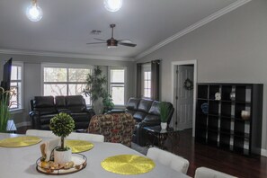Una sala de estar con ventilador de techo, dos sofás de cuero negro, una mesa de centro y un aparador de vidrio con objetos decorativos.