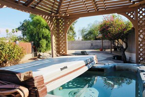 Un jacuzzi bajo una pérgola de madera, con un muro de ladrillo y árboles al fondo.