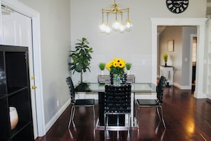 A dining area with a glass table, black chairs, a chandelier, and a clock on the wall.