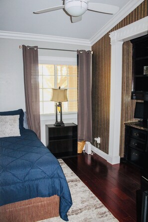 A bedroom with a bed, a nightstand, a lamp, a window with curtains, and a television.