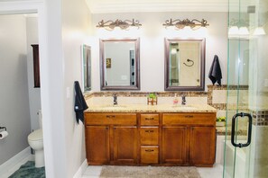 Un baño con lavamanos doble, dos espejos, cabina de ducha de vidrio y barra para toallas.