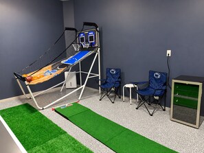 A basketball hoop with a net, two blue folding chairs, a small white table, and a green artificial turf area.