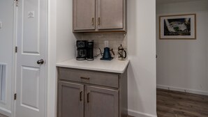 A kitchen with a coffee maker, a kettle, and a framed picture on the wall.