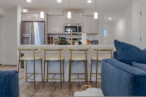 A modern kitchen with stainless steel appliances, a central island with bar stools, and a blue sofa in the foreground.