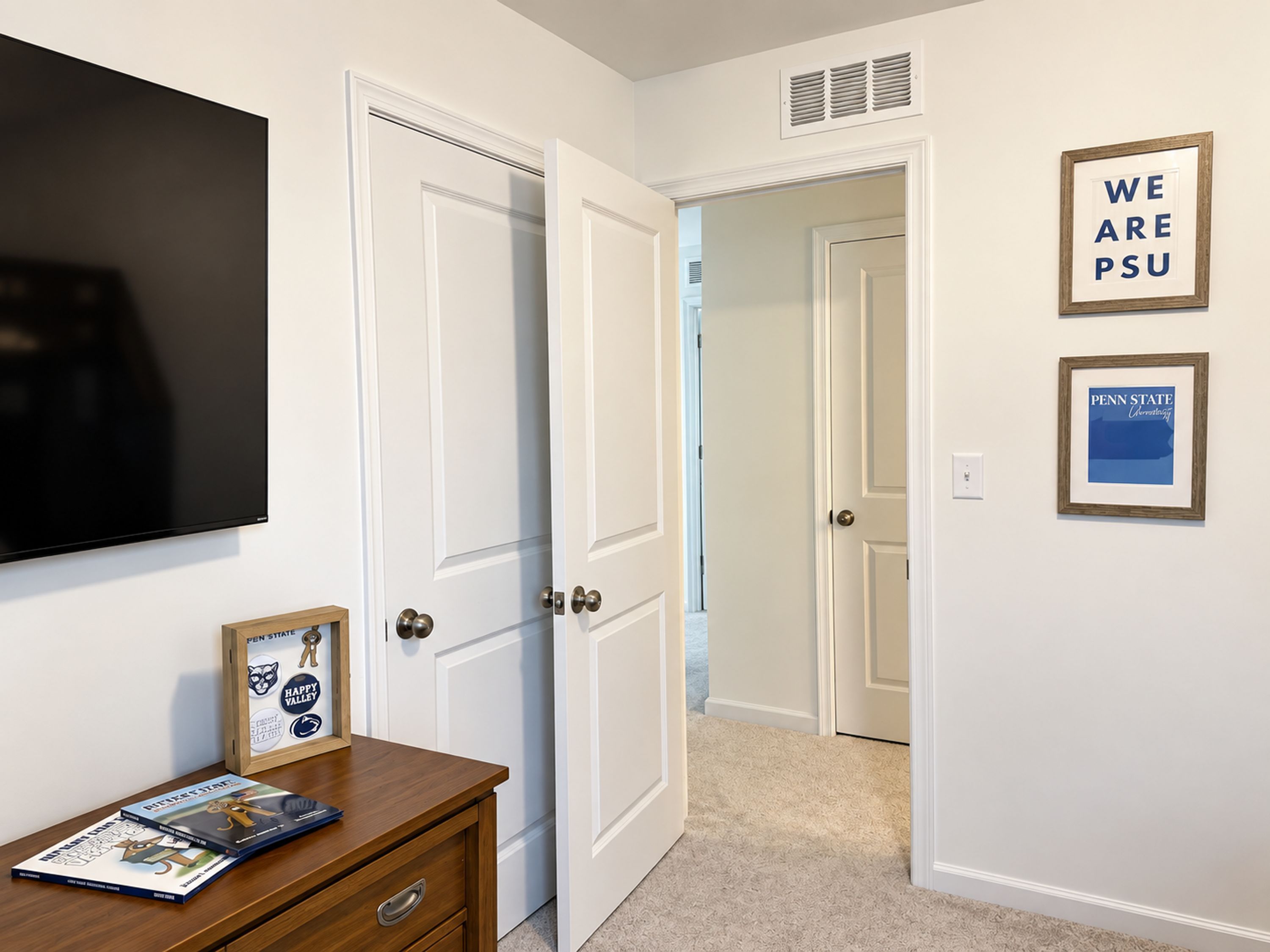 A hallway with white doors, a mounted television, and framed posters on the wall.