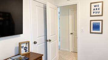 A hallway with white doors, a mounted television, and framed posters on the wall.