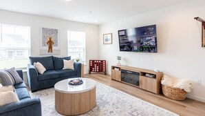 Un salon moderne avec un canapé bleu, une table basse ronde et un téléviseur à  écran plat fixé au mur.
