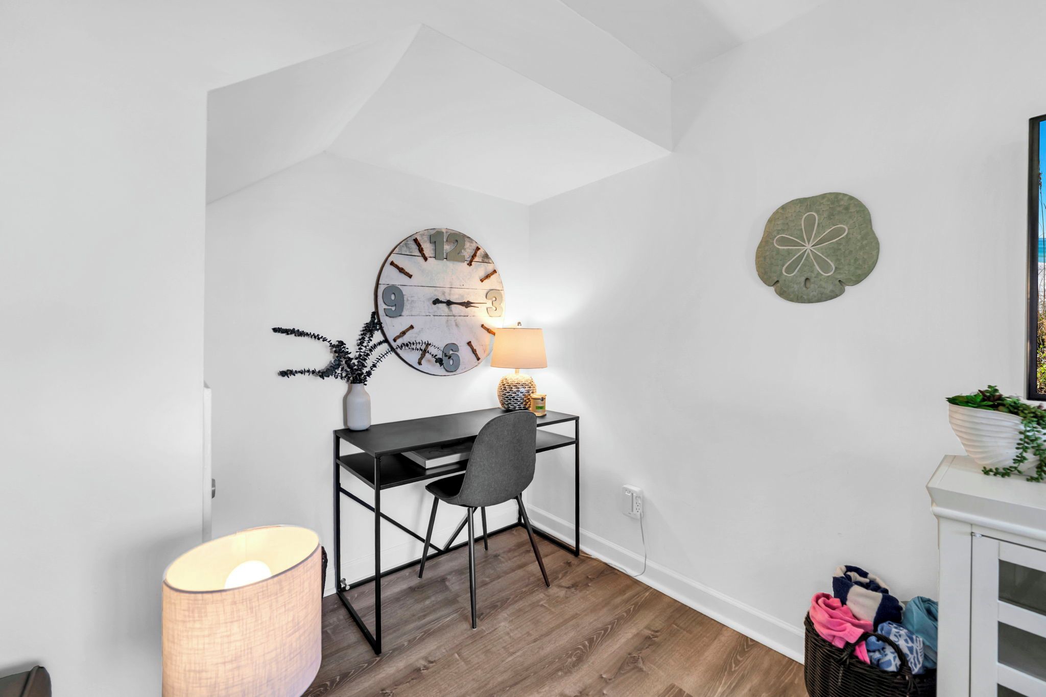 Una habitación con escritorio, silla, lámpara y un reloj de pared.