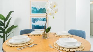 Un comedor con una mesa redonda, platos blancos y un centro de mesa con orquídeas blancas.