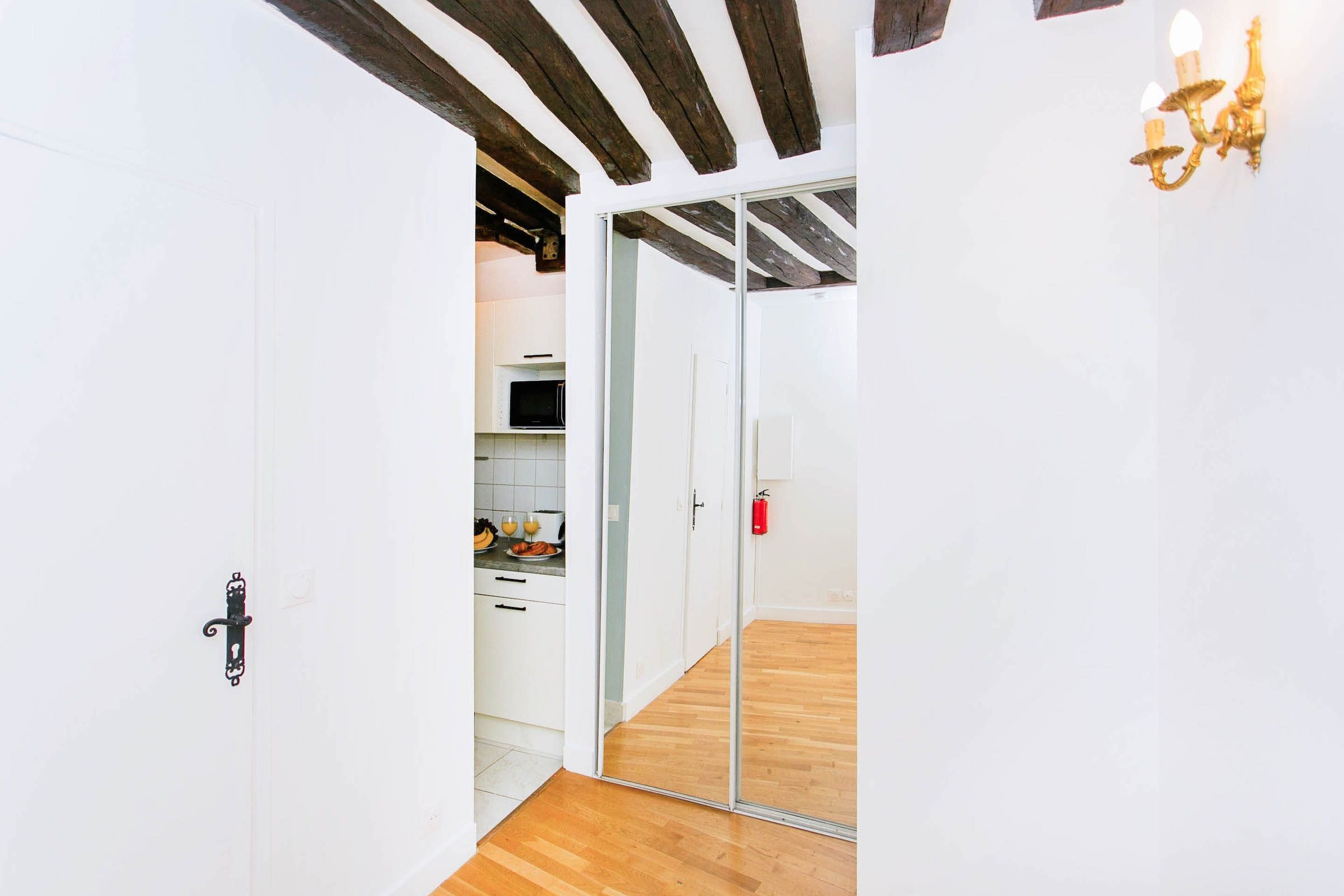 A hallway with a wooden floor, white walls, and a sliding glass door leading to a kitchen area.