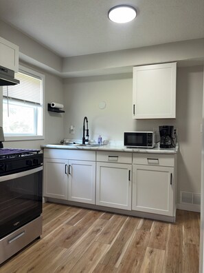 Una cocina moderna con armarios blancos, horno empotrado, microondas y cafetera.