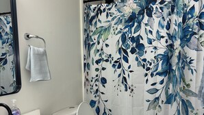 A bathroom with a white sink, a toilet, a shower curtain with a floral pattern, and a blue bath mat. - Cozy, contemporary apartment outside of the Fort Wayne city center (Fort Wayne)