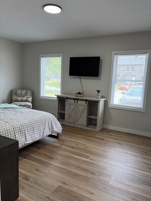 Un dormitorio con una cama, un televisor montado en la pared y una ventana con persianas.